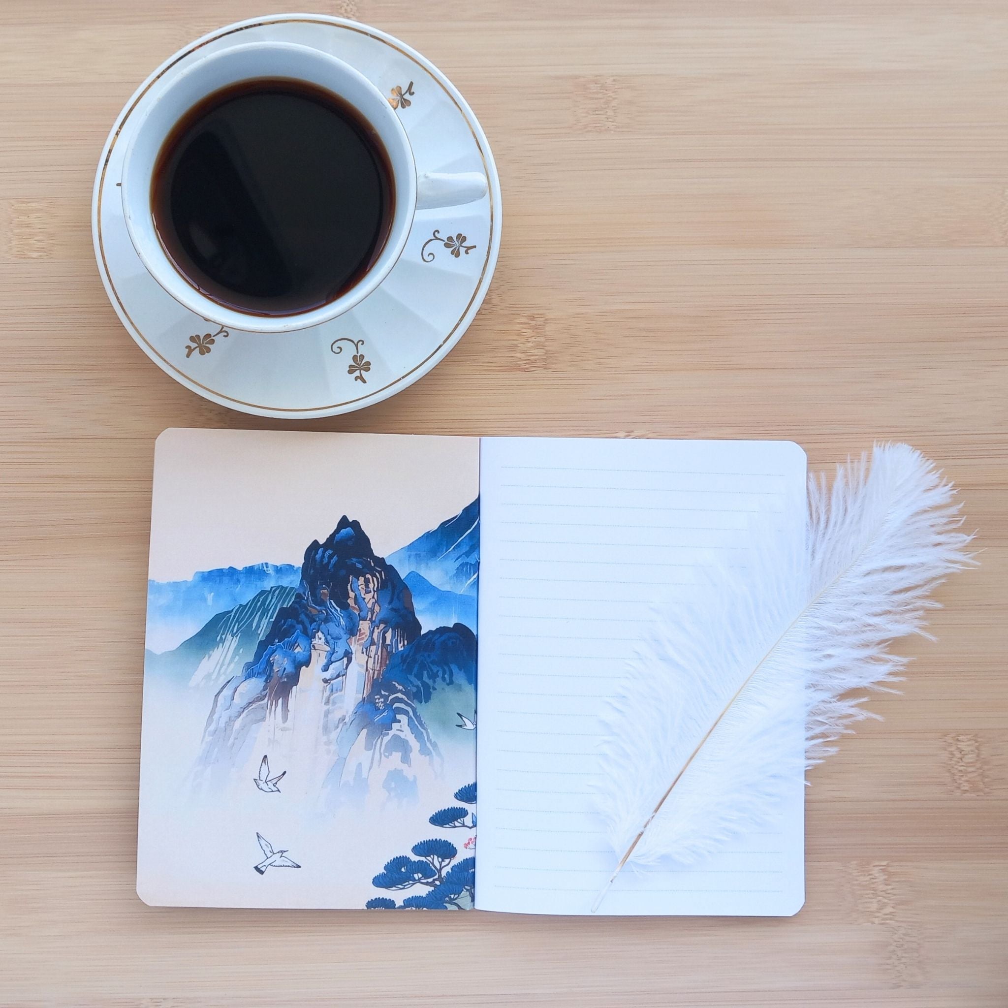 Vue ouverte sur la couverture intérieure arrière du carnet de notes A6 fait main, montrant la reliure dos carré agrafé et les pages. La page de garde arrière de gauche présente une illustration d'inspiration estampe japonaise d'un pic montagneux bleu et vert avec des oiseaux en vol.