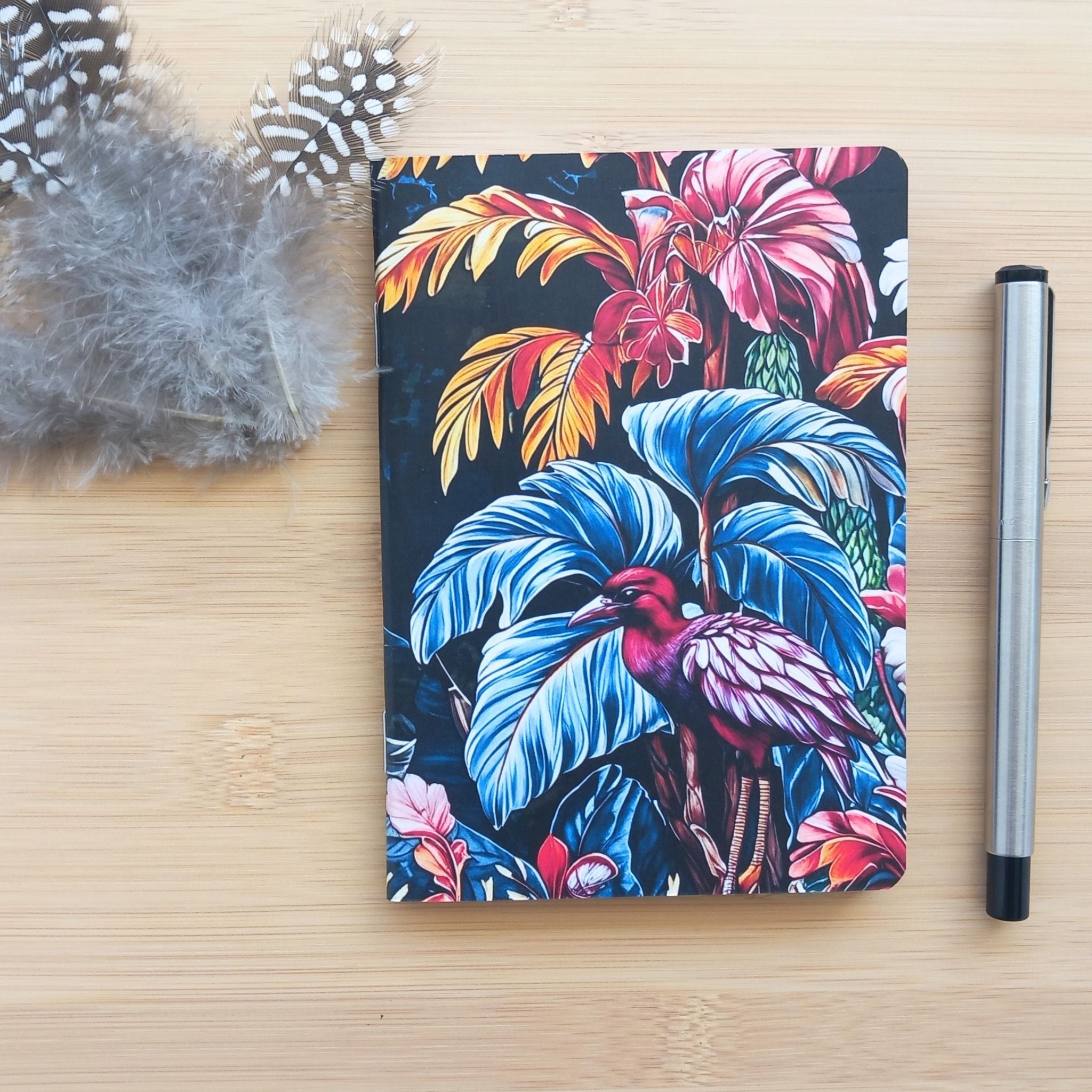 Première de couverture du carnet de notes A6 artisanal, illustrée d'une végétation exotique dense bleu sarcelle et vieux rose, avec un oiseau tropical amarante et magenta.