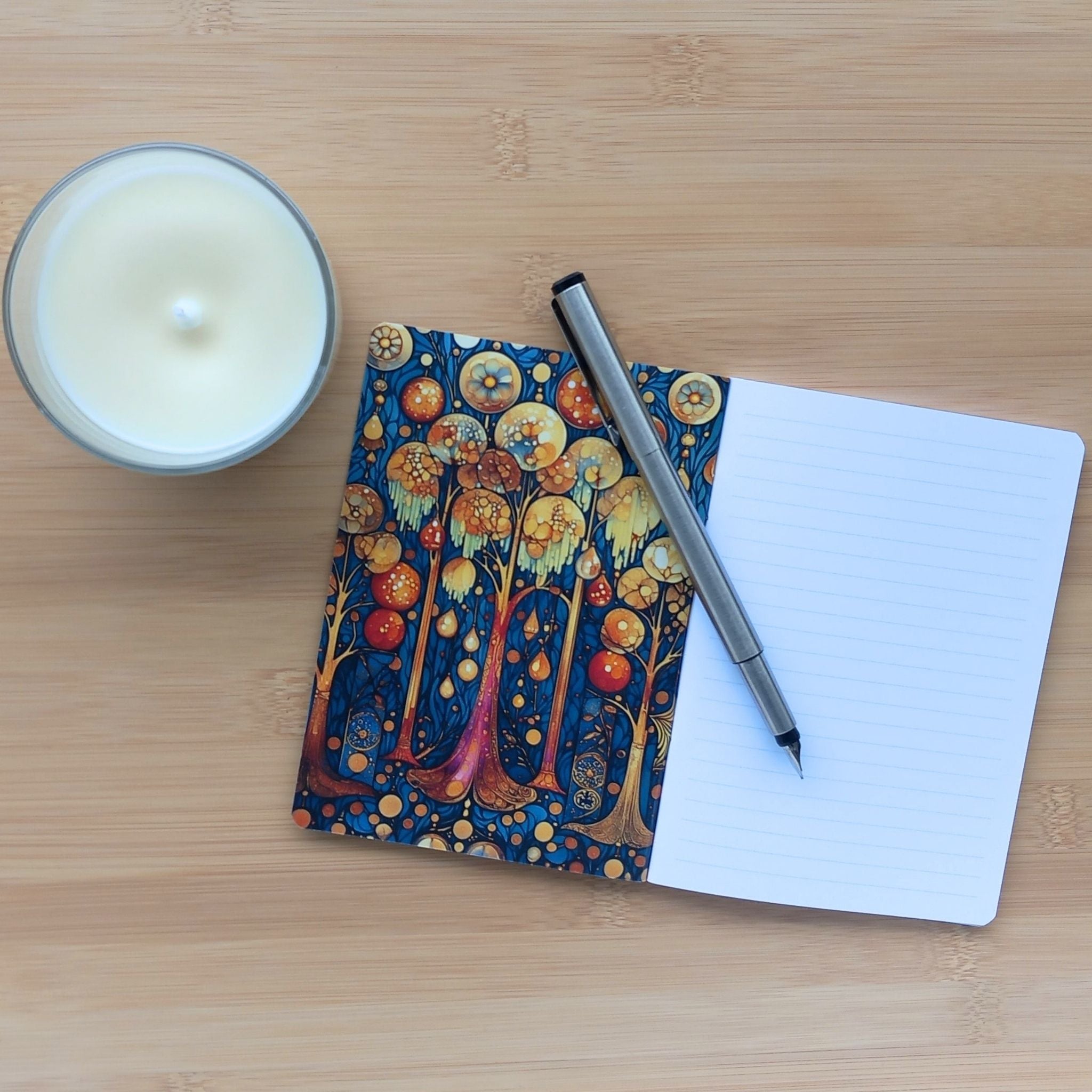 Carnet artisanal A6 ouvert avec un stylo sur des pages lignées. La couverture intérieure gauche révèle un décor magique d'arbres dorés lumineux.