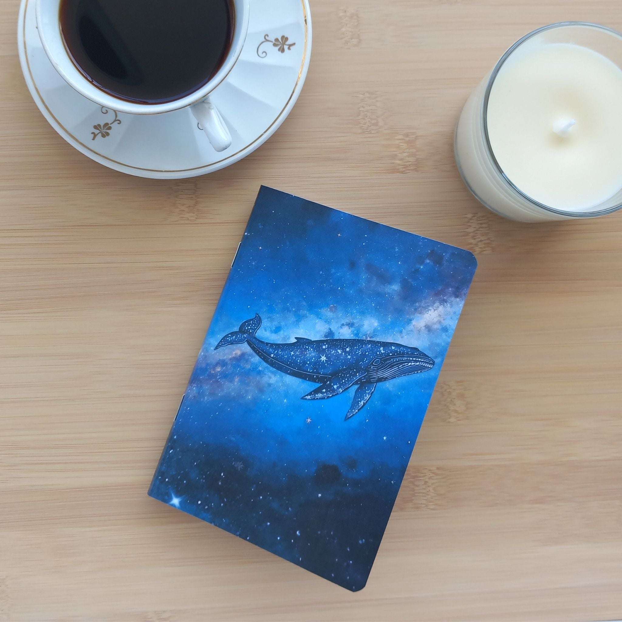 Petit bloc-notes artisanal sur le thème de l'astronomie posé à plat. Focus sur le design de la face avant : la silhouette détaillée d'une baleine cosmique remplie d'étoiles, flottant au cœur de la Voie Lactée.