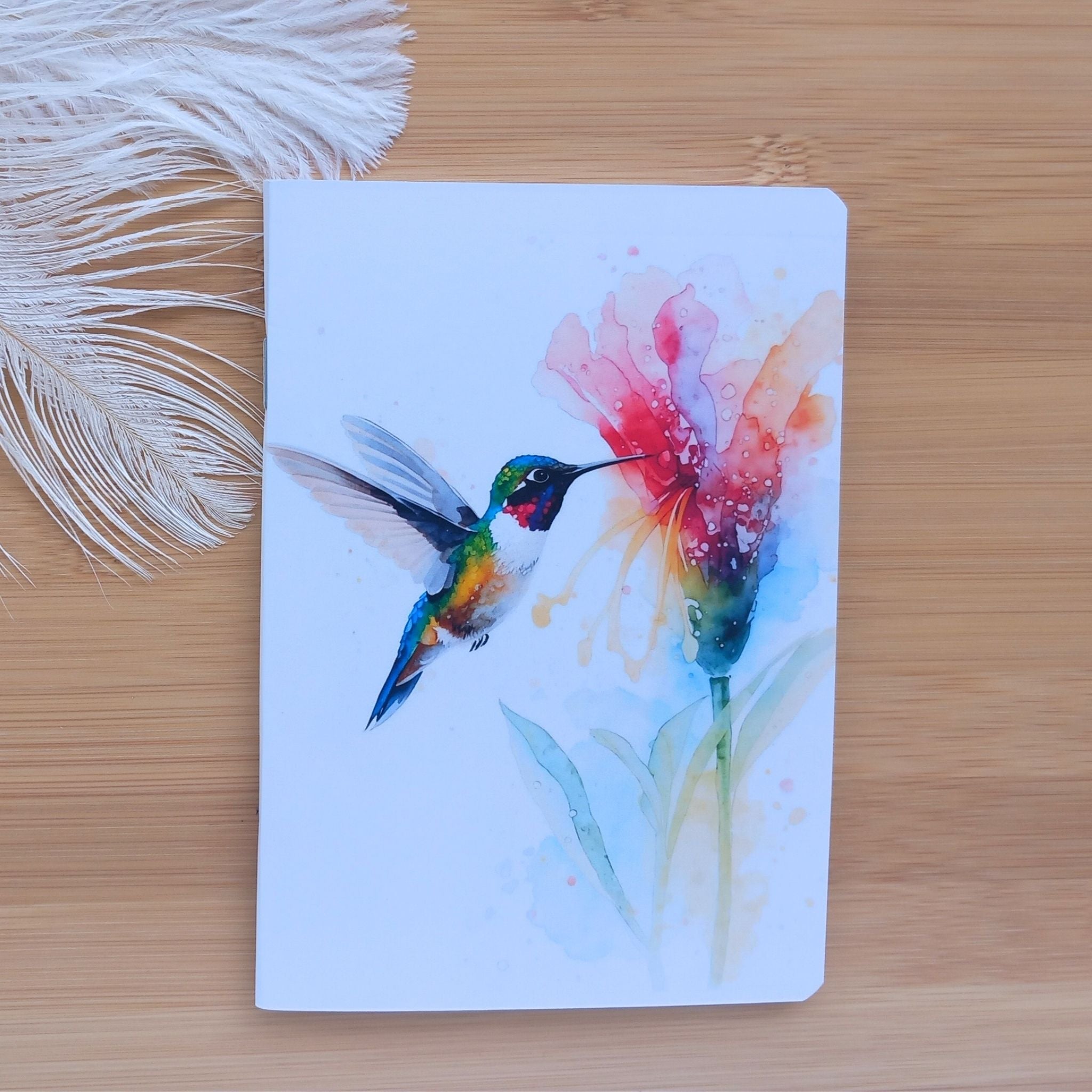 Première de couverture du carnet de notes A6 illustrée à l'aquarelle, représentant un colibri coloré en vol s'approchant d'une fleur rose et pêche.